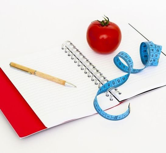 cuaderno con un tomate, un metro y un bolígrafo 